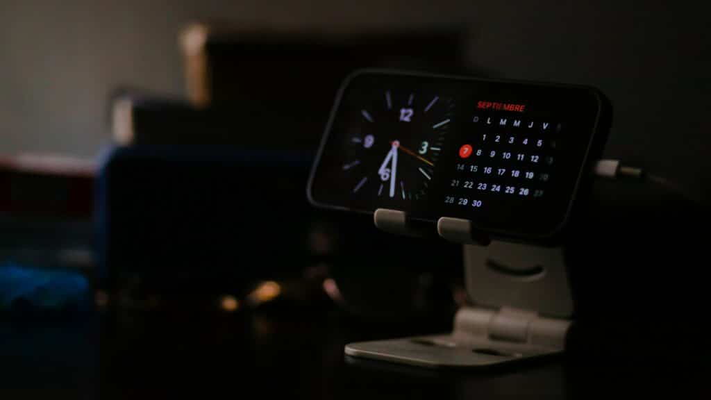 Smartphone displaying clock and calendar on stand.