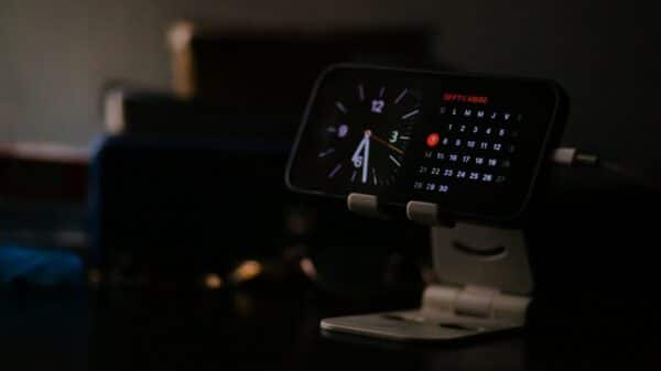 Smartphone displaying clock and calendar on stand.
