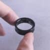 Fingers hold a black smart ring with circuits visible.