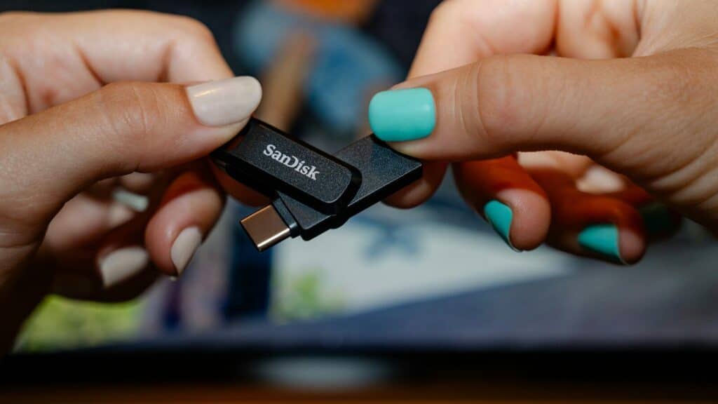 Two hands holding a sandisk usb flash drive.