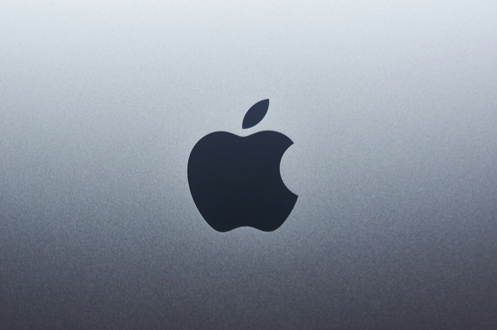 A dark apple logo centered on a smooth grey metallic surface